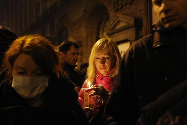 Woman holds a candle as she attends the transfer of over a dozen of corpses from a hotel lobby to a local hospital following clashes with riot police at Independence Square in Kiev