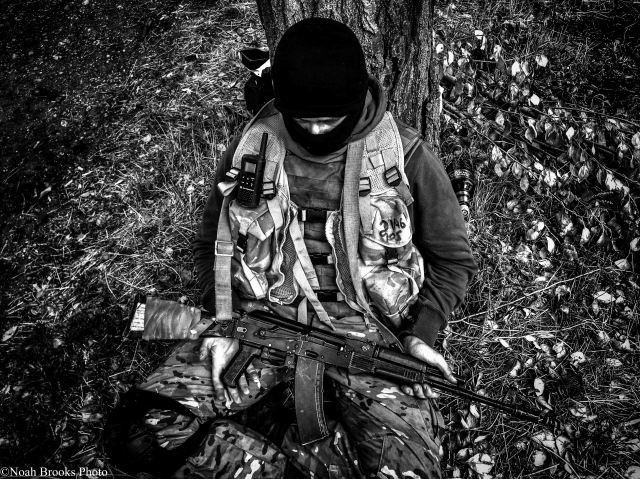 A soldier waiting at a block post behind some trees near Mariupol while continued shelling targets their position. Photo: Noah Brooks